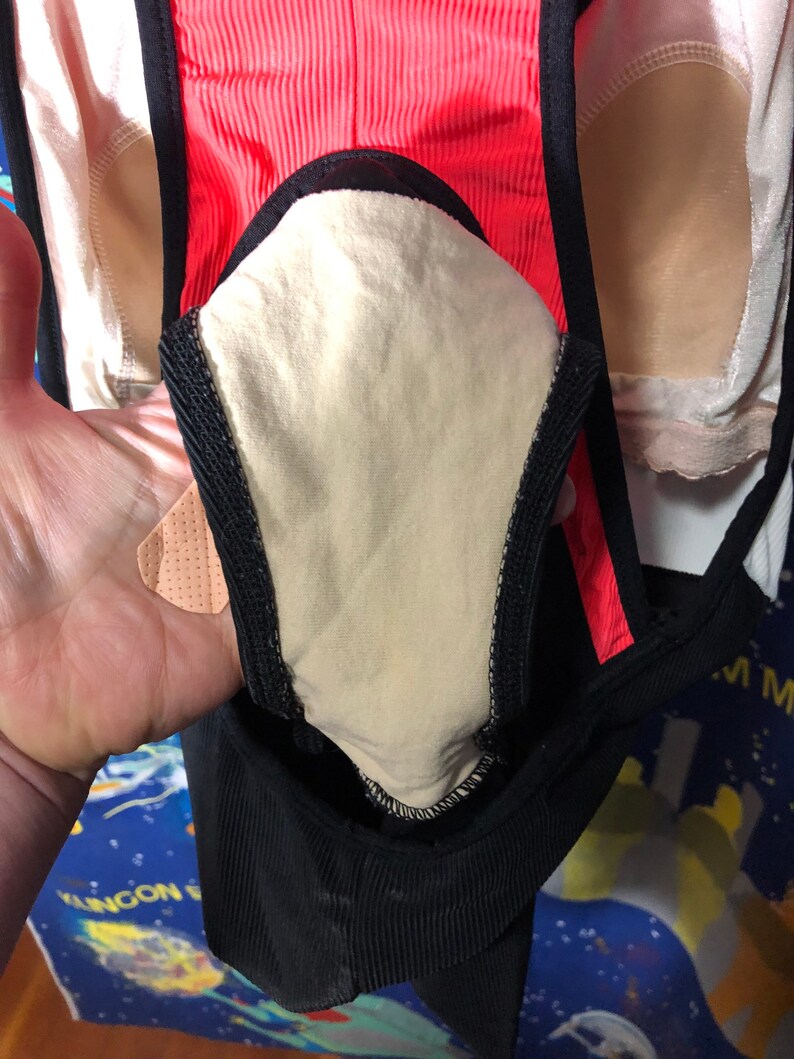 May include: Close-up of a black and coral athletic garment with a beige interior lining. The garment has a ribbed texture and black trim. The image shows a portion of the garment, highlighting its design and construction.