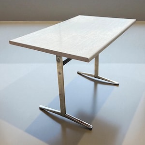 May include: A rectangular table with a light wood grain top and brushed metal legs. The table has a minimalist design, with the legs forming a T-shape at the base. The table is approximately 76 cm long and 46 cm wide.