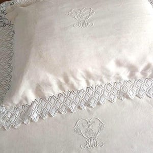 May include: Ivory-colored bedding set featuring a pillow and sheet. The pillow and sheet are adorned with delicate white embroidered floral designs and lace trim. The bedding set is made of a soft, possibly linen, material.
