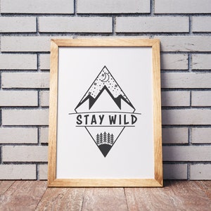 Puede incluir: Una impresi&oacute;n enmarcada con una ilustraci&oacute;n en blanco y negro de una cordillera con una luna creciente y estrellas. El texto "STAY WILD" est&aacute; escrito en una pancarta debajo de las monta&ntilde;as.