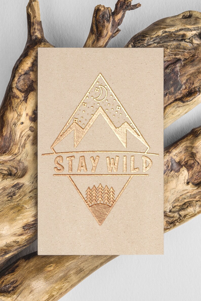 Puede incluir: Un dise&ntilde;o estampado en l&aacute;mina dorada sobre un fondo de cartulina marr&oacute;n. El dise&ntilde;o presenta una cordillera, una luna creciente, estrellas y el texto "STAY WILD".