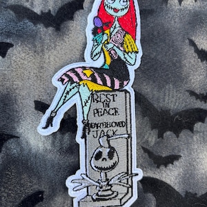 May include: Embroidered patch featuring Sally from The Nightmare Before Christmas, sitting on a tombstone that reads "Rest in Peace, Jack, my beloved." Sally has red hair, a patchwork dress, and holds flowers. The tombstone has a Jack Skellington design.
