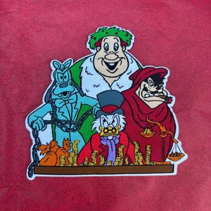 May include: A colorful patch featuring four cartoon characters. Scrooge McDuck is in the center, surrounded by other characters, including Goofy. The characters are set against a red background.