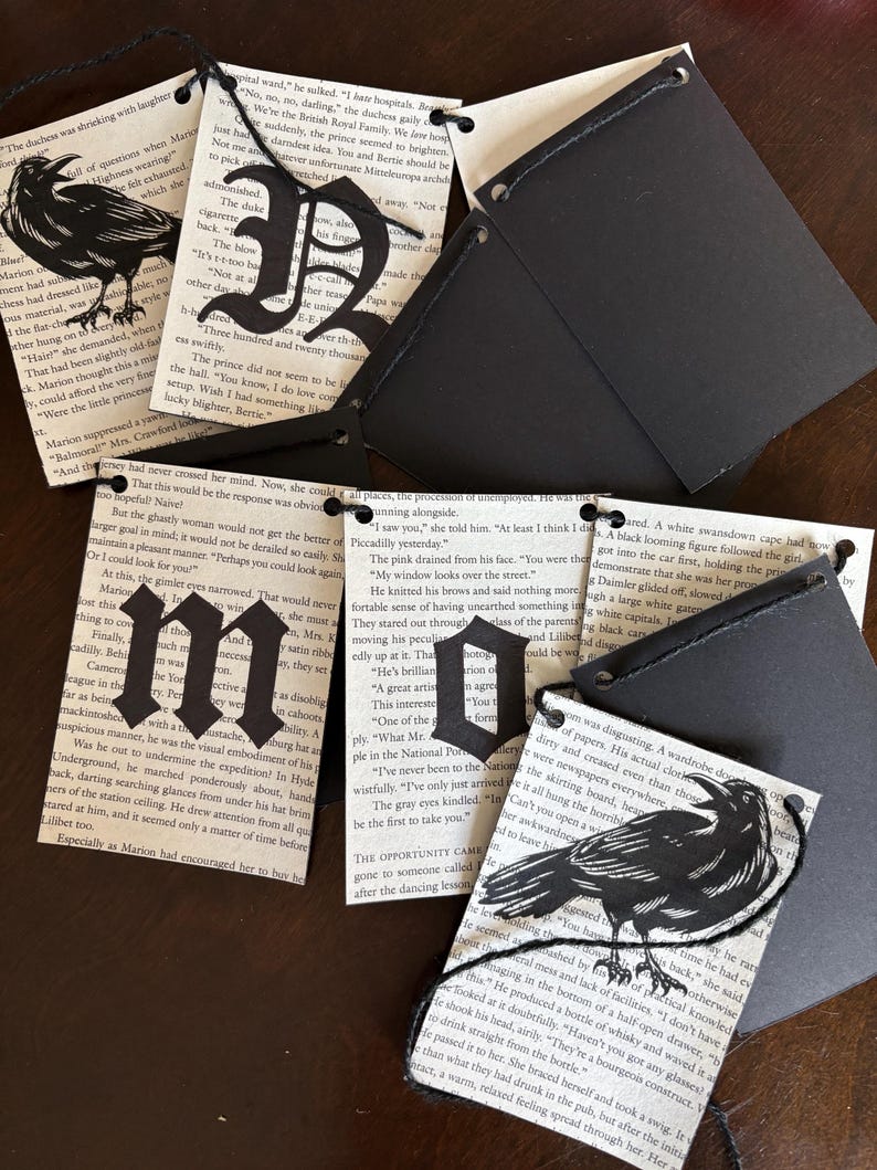 May include: Black paper tags with cut-out letters and raven silhouettes. The tags are attached to pages from a vintage book. The letters spell out words and phrases. The tags are connected with black string.
