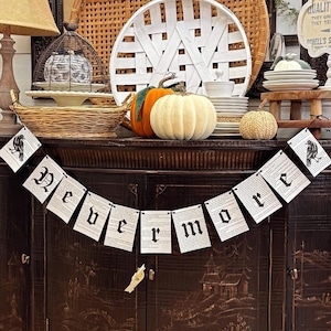 May include: A decorative Halloween display featuring a banner that reads "Nevermore" with raven illustrations. The display includes pumpkins, decorative plates, and a woven basket. The color palette is autumnal, with warm tones and a vintage aesthetic.