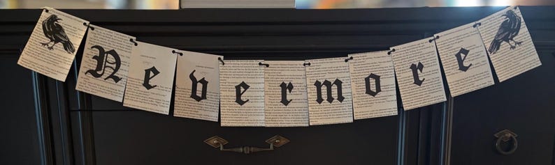 May include: A banner with the word "Nevermore" printed in black gothic font on pages of text. The banner is decorated with illustrations of black crows on each end. The banner is hanging on a dark surface.