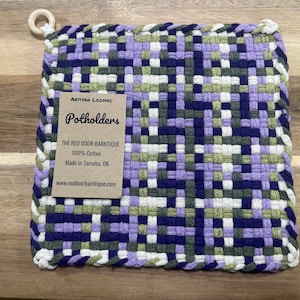 May include: Purple, green, white, and blue woven cotton potholder with a brown label that reads "Artisan Loomed Potholders The Red Door Barntique 100% Cotton Made in Tamaha, OK www.reddoorbarntique.com"