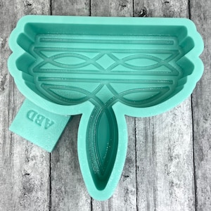 May include: A light green silicone mold shaped like a stylized flower with a geometric pattern. The mold has a label that says "ABD".