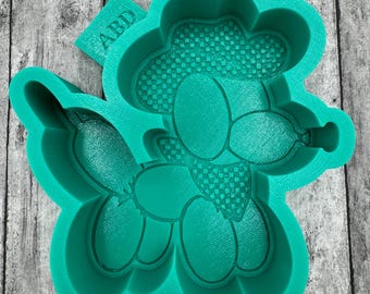 May include: A teal silicone mold in the shape of a poodle wearing a bow tie and hat. The hat and bow tie have a checkered pattern. The mold has the letters "ABD" on a small tab.