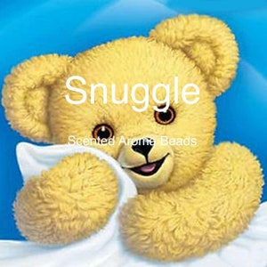 May include: A yellow teddy bear with a white blanket, smiling and looking at the camera. The text "Snuggle Scented Aroma Beads" is printed on the image.
