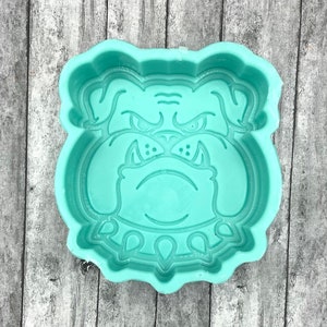 May include: A teal blue silicone mold shaped like a bulldog's head. The mold has a detailed design of the bulldog's face, including its eyes, nose, and teeth.