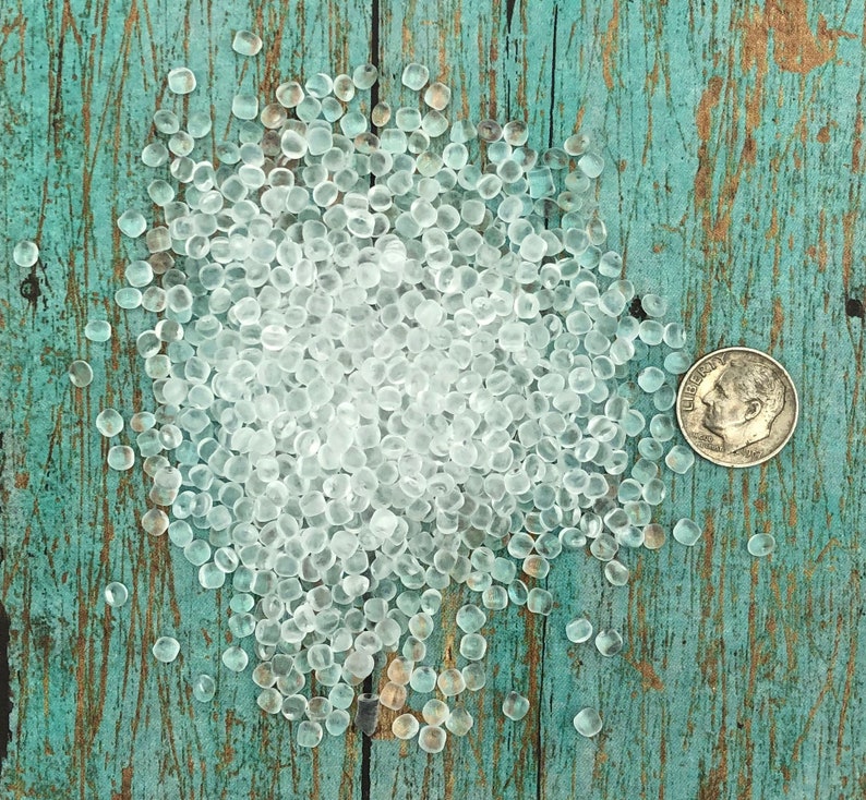 May include: A large pile of clear, translucent, round beads on a blue and green wooden surface. The beads are small and uniform in size.