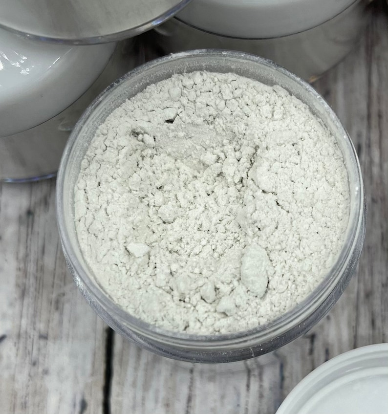 May include: A close-up view of a clear plastic container filled with a white powder. The powder is finely ground and has a slightly grainy texture.