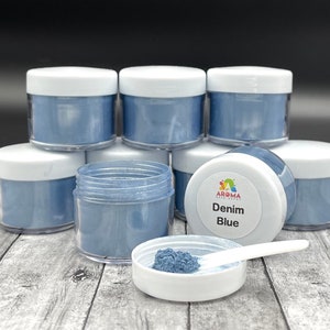May include: Eight small jars of blue food coloring powder, stacked in a pyramid shape. The jar in the front has a white label that reads "Aroma Food Craft Denim Blue".
