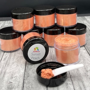 May include: Eight small jars of orange shimmer powder with black lids. The label on one jar reads "Aroma Sunset Peach".