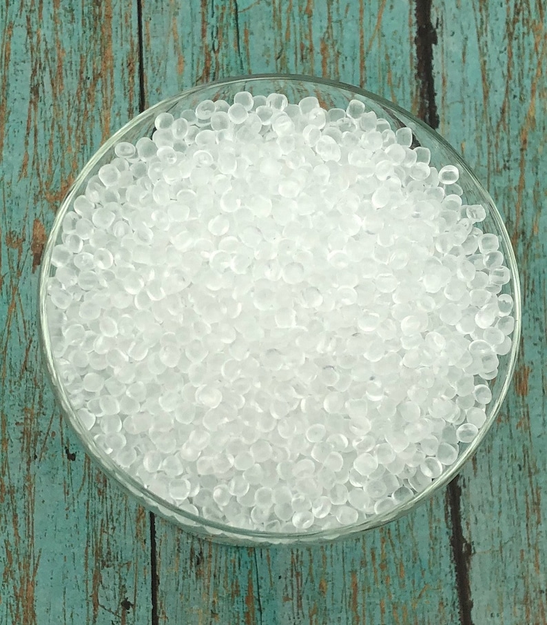 May include: A clear glass bowl filled with small, white, translucent beads. The beads are uniform in size and shape, and they are arranged in a random pattern.