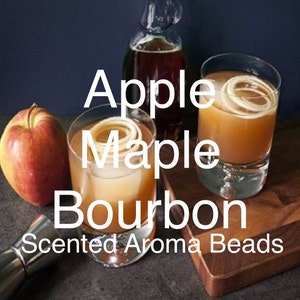 May include: Two glasses of amber liquid with ice and apple slices, a bottle of maple syrup, and a red apple. The text "Apple Maple Bourbon Scented Aroma Beads" is displayed on a wooden surface.