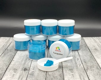 May include: Eight small jars of turquoise blue mica powder, with one jar open and a scoop of powder in a white dish. The label on the open jar reads "Aroma Extracts Turquoise".