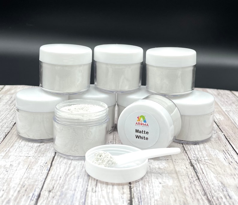 May include: A set of seven small white jars filled with white powder. The jars are labeled "Matte White" and have a rainbow logo. The jars are on a wooden surface.