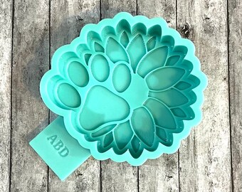 May include: A light blue silicone mould with a paw print design inside a sunflower shape. The mould has the letters "ABD" on the side.
