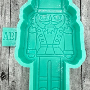 May include: A green silicone mold shaped like a nutcracker. The mold has a detailed design of a nutcracker with a hat, mustache, and buttons.