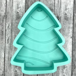 May include: A light green silicone mold shaped like a Christmas tree. The mold has a textured surface with lines that resemble a tree trunk.