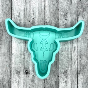 May include: A teal blue silicone mold shaped like a bull skull with a geometric design in the center. The mold is perfect for making resin crafts.