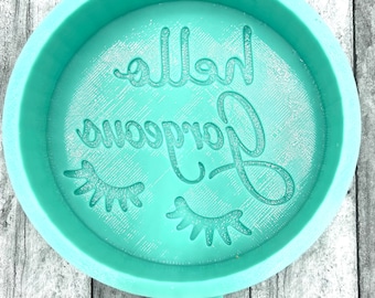 May include: A teal blue silicone mold with the text "Hello Gorgeous" and two eyelashes. The mold has a label on the bottom that says "ABD".