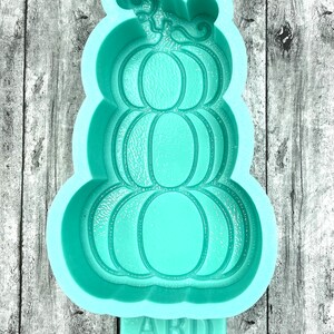 May include: A teal blue silicone mold shaped like a stack of three pumpkins with a swirl design on top. The mold has the letters "ABD" at the bottom.