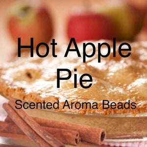 May include: A close-up of a golden brown apple pie with a flaky crust and a dusting of powdered sugar. The pie is surrounded by cinnamon sticks and the text "Hot Apple Pie Scented Aroma Beads" is displayed above the pie.