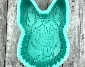 May include: A teal silicone mold in the shape of a German Shepherd dog's head. The mold has detailed facial features, including eyes, nose, and a tongue sticking out. The mold is designed for crafting and creating dog-themed items.