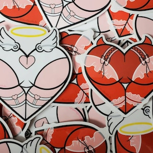 May include: A set of stickers featuring two different heart-shaped designs. One heart is red with devil horns and wings, and the other is pink with angel wings and a halo. Both hearts are wearing lingerie.