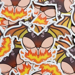 May include: A stack of colourful stickers featuring a cartoon illustration of a dragon's rear end with fire coming out of the bottom. The dragon is brown and orange with purple horns. The stickers are on a white background.