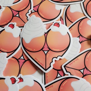 Puede incluir: Un conjunto de pegatinas en forma de corazón rosa y blanco con un diseño de crema batida y cereza. Las pegatinas tienen el texto "@deaththatbabe" en ellas.