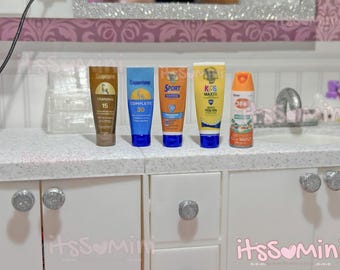 Könnte beinhalten: Eine Sammlung von Miniatur-Sonnencreme- und Insektenschutzmittel-Tuben und -Flaschen. Die Produkte umfassen Coppertone Tanning 15, Complete 30, Sport 30, Kids Max und Off! Die Tuben sind braun, blau, orange und gelb.