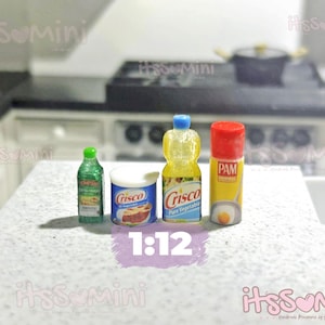 May include: Miniature kitchen supplies including a green bottle, a white container of Crisco, a yellow bottle of Crisco Pure Vegetable Oil, and a PAM cooking spray can. The items are arranged on a white countertop. The scale is 1:12.