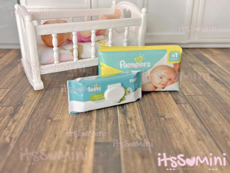 May include: A miniature white wooden crib with a baby doll inside, next to a package of Pampers diapers and a package of baby wipes. The Pampers package is yellow and teal, and the wipes package is teal and white.