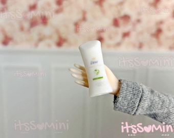 Könnte beinhalten: Ein weißer Deodorant-Stick mit dem Dove-Logo und einem grün-weißen Etikett. Das Produkt wird von einer Hand mit einem grauen Pulloverärmel im Hintergrund gehalten.