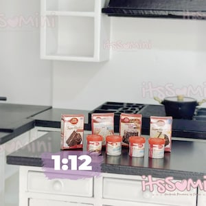 May include: Miniature kitchen scene with a black countertop, white cabinets, and shelves. Includes miniature cake mix boxes, small jars, a stove, and a pot. The text "1:12" is visible.