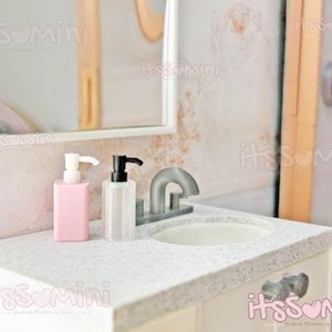 May include: A white countertop with a white porcelain sink and two soap dispensers. One dispenser is pink and the other is clear. A silver faucet is visible in the background.