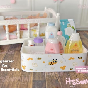 May include: A white organizer with a bee and cloud pattern, holding baby essentials. The organizer contains bottles, a diaper pack, and other baby care items. A white crib is in the background.
