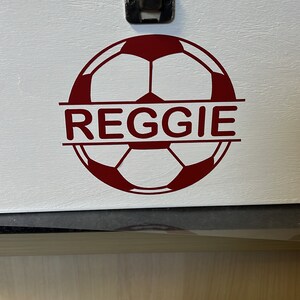 May include: White wooden box with a red soccer ball design and the name "REGGIE" printed across the ball. The box has a metal latch.
