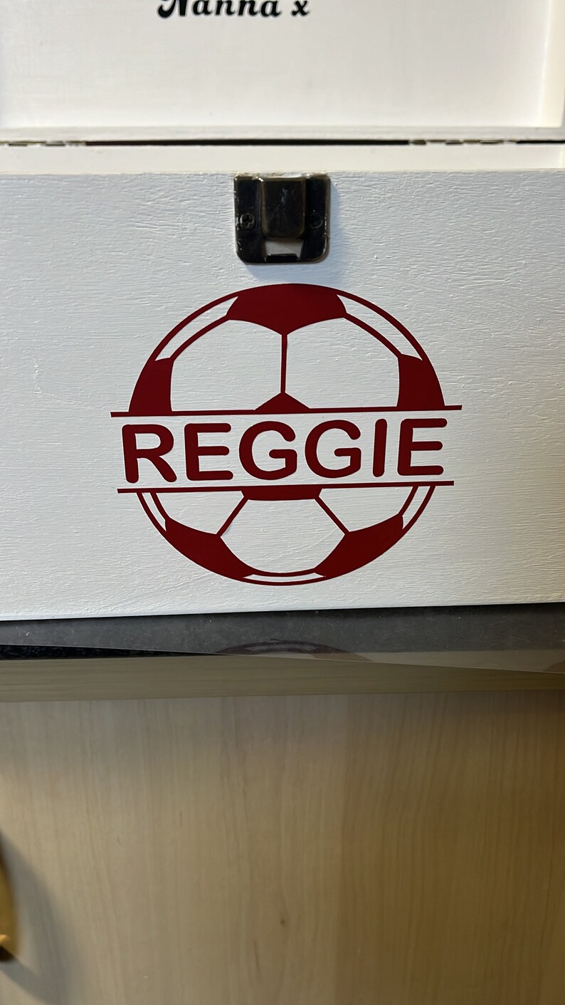 May include: White wooden box with a red soccer ball design and the name "REGGIE" printed across the ball. The box has a metal latch.