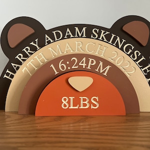 May include: A wooden bear-shaped baby announcement plaque with a rainbow design. The plaque is decorated with the name "Harry Adam Kingsley", the date "7th March 2022", the time "16:24PM", and the weight "8 LBS".