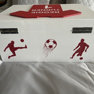 May include: White wooden box with a red top that says "REGGIE TURNER #1". The box has two silver hinges and is decorated with red soccer player silhouettes and a soccer ball.