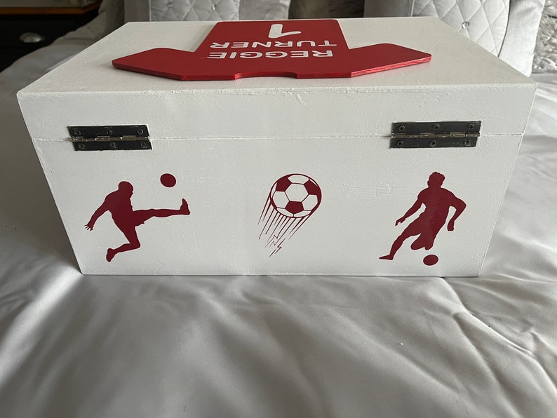 May include: White wooden box with a red top that says "REGGIE TURNER #1". The box has two silver hinges and is decorated with red soccer player silhouettes and a soccer ball.