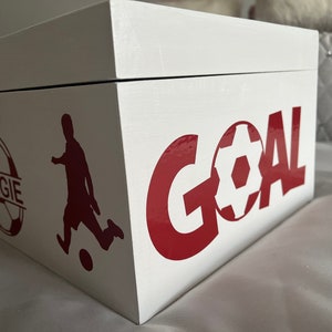 May include: White wooden box with a red and white soccer ball design. The box has the word "GOAL" written in red letters and a soccer player silhouette. The soccer ball has the name "REGGIE" written on it.