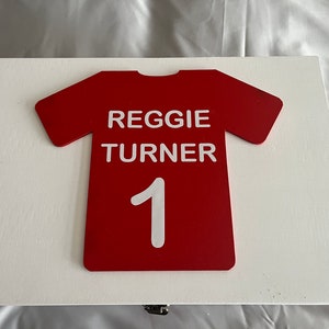 May include: A white wooden box with a red jersey design on the front. The jersey has the name "REGGIE TURNER" and the number "1" on it.