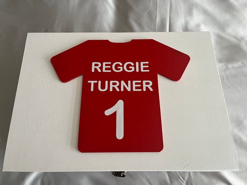 May include: A white wooden box with a red jersey design on the front. The jersey has the name "REGGIE TURNER" and the number "1" on it.