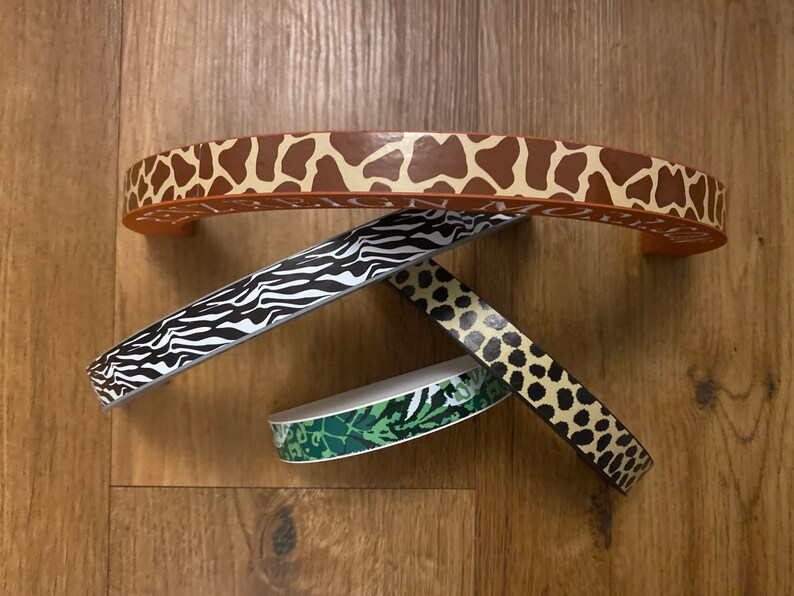 Puede incluir: Cuatro piezas de adorno de tela con diferentes patrones. Una pieza es marr&oacute;n con estampado de jirafa, otra es blanco y negro con estampado de cebra, otra es verde con estampado de camuflaje y otra es marr&oacute;n con estampado de leopardo.